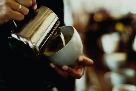 Milk is poured from a metal jug into a cup of coffee.